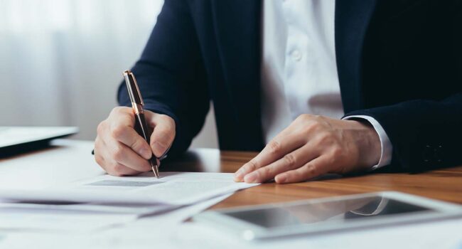 Close-up photo of businessman's hands signing documents at desk, man at work in business suit